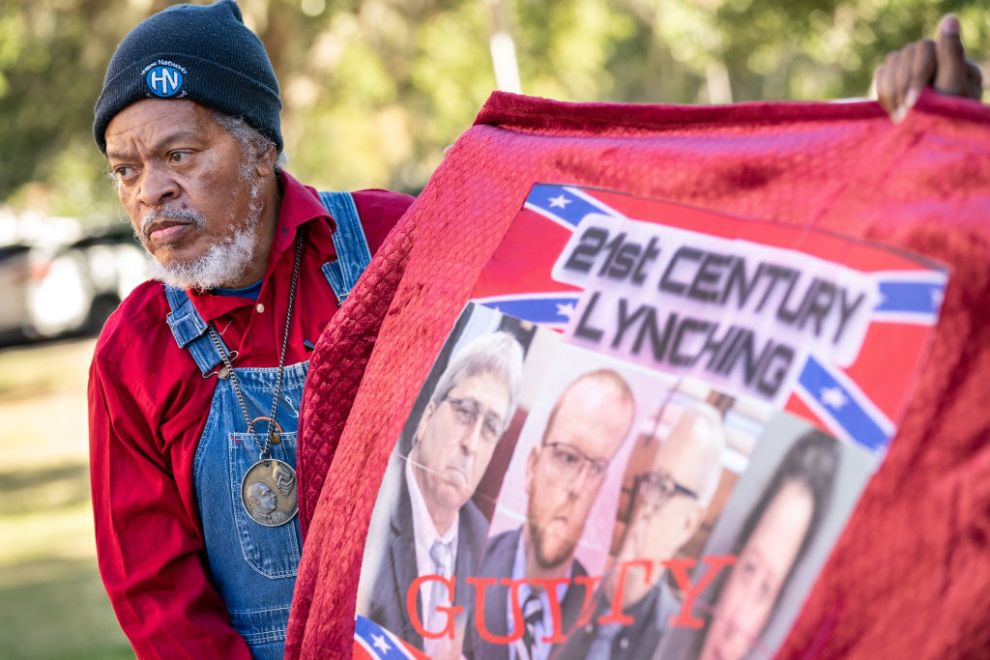 BRUNSWICK, GA - NOVEMBER 24: Eric Terrell, vice president of the National Action Network, holds a banner with photos of William Roddie Bryan, Travis McMichael, Greg McMichal and former Brunswick District Attorney Jackie Johnson outside the Glynn County Courthouse as the jury deliberates in the trial of the killers of Ahmaud Arbery on November 24, 2021 in Brunswick, Georgia. Greg McMichael, his son Travis McMichael, and a neighbor, William "Roddie" Bryan are charged with the February, 2020 fatal shooting of 25-year-old Ahmaud Arbery.
